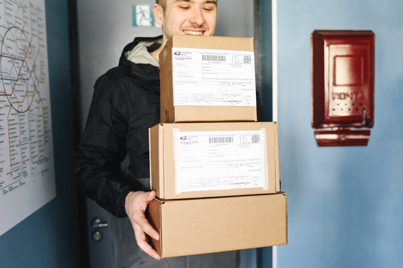Smiling delivery man holding packages inside a building, ready for delivery.